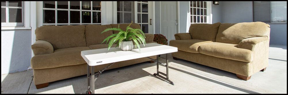An outdoor patio area with a sofa and armchair, featuring a white coffee table adorned with a potted fern.