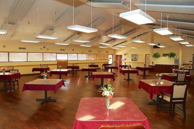 A spacious dining hall with neatly arranged tables and chairs, featuring a wooden floor and ambient lighting.