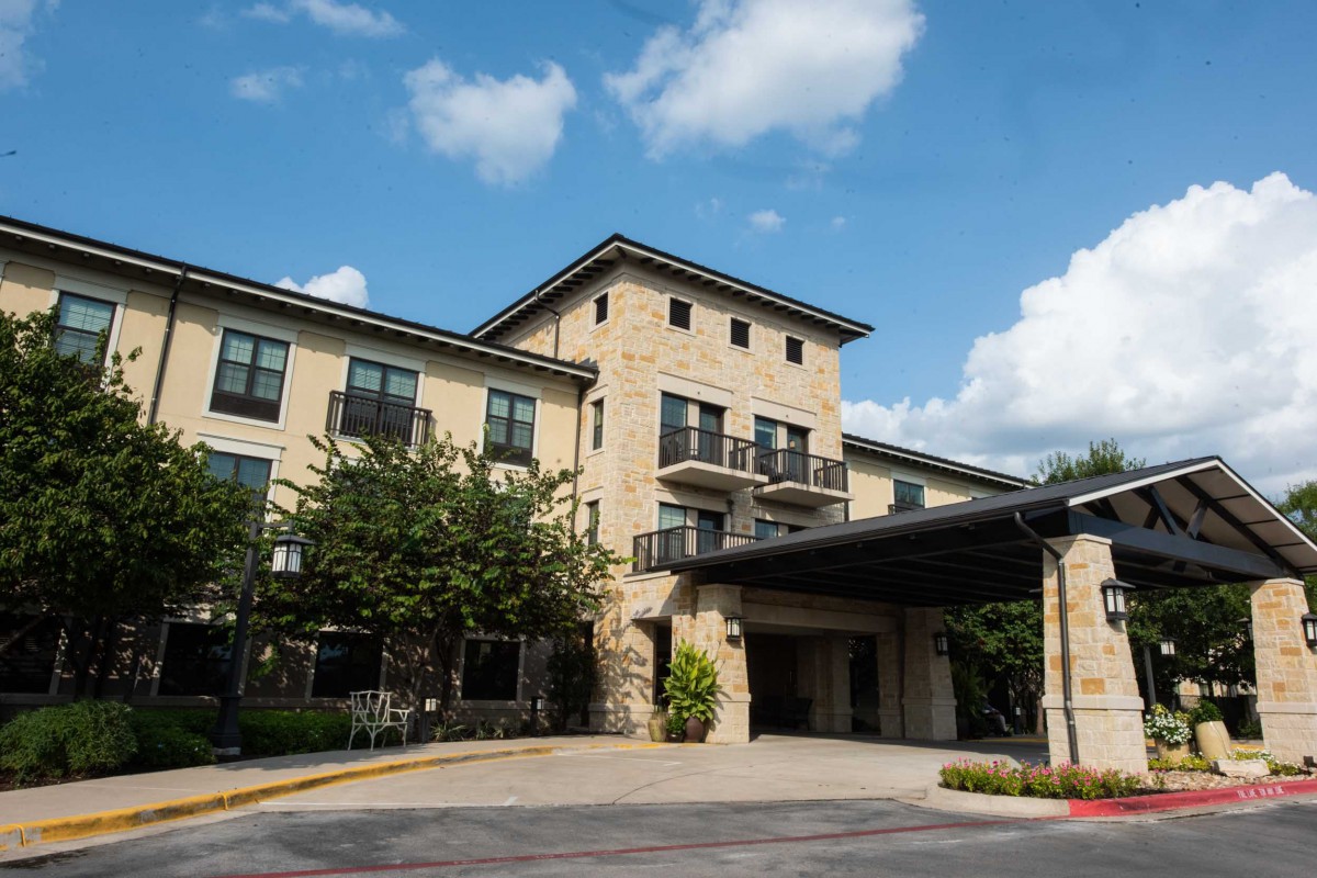 A modern hotel building with stone exterior under a blue sky with clouds.