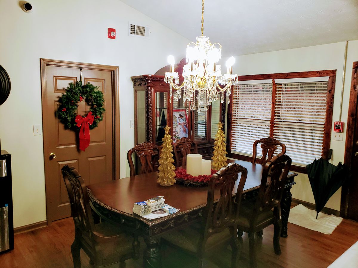 A warmly decorated dining room with a chandelier, featuring holiday accents such as a wreath and festive table centerpiece.