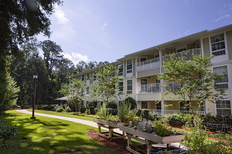 A well-maintained apartment complex surrounded by gardens and trees on a sunny day.