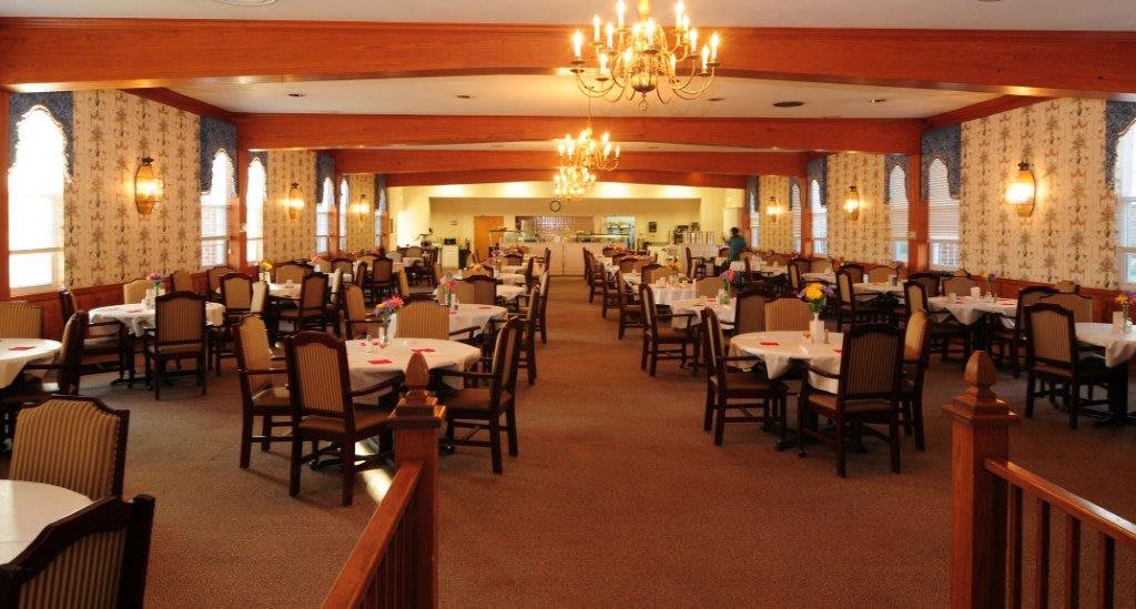 A spacious dining room with neatly arranged tables and chairs, illuminated by chandeliers.