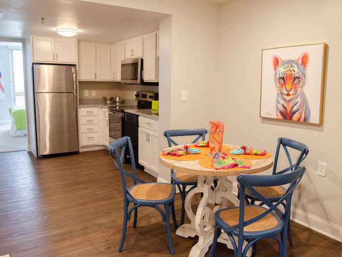 A modern kitchen and dining area with a round table, blue chairs, and stainless steel appliances.