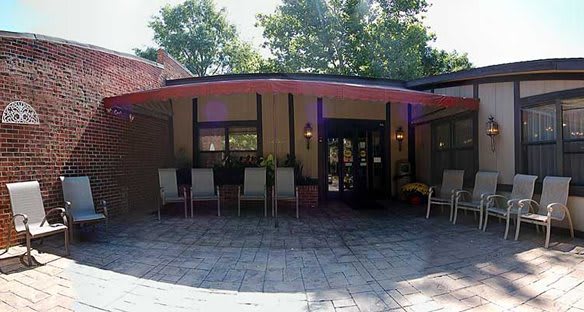 A patio area with several chairs in front of a building entrance, surrounded by trees.