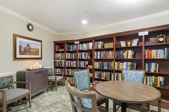 A cozy library room with bookshelves, chairs, and a table.