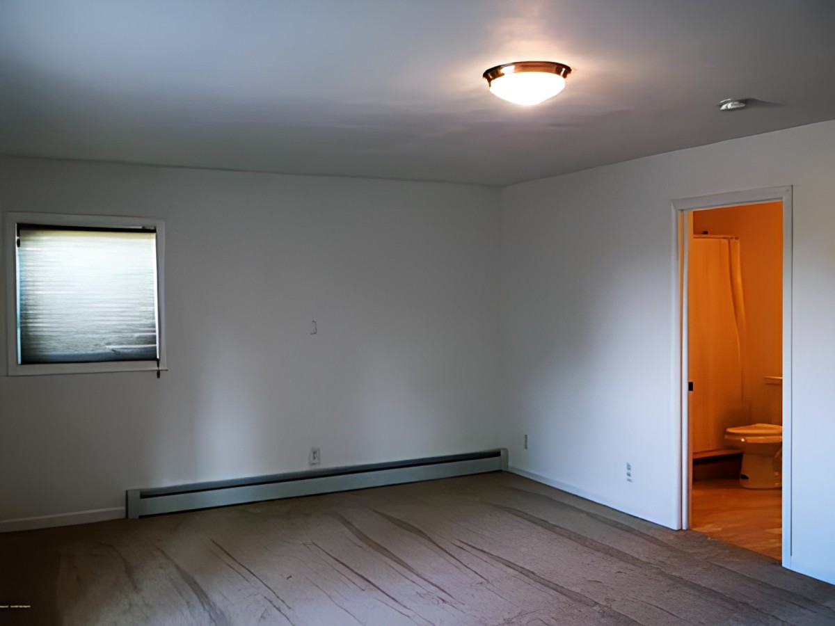An empty room with a window, light fixture, and beige carpet.