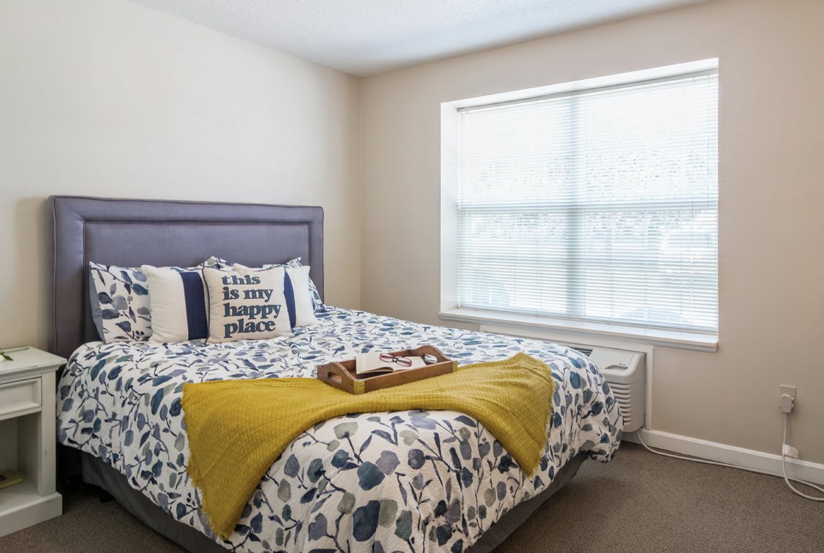 A cozy bedroom with a floral-patterned bed, decorative pillows, and a large window letting in natural light.