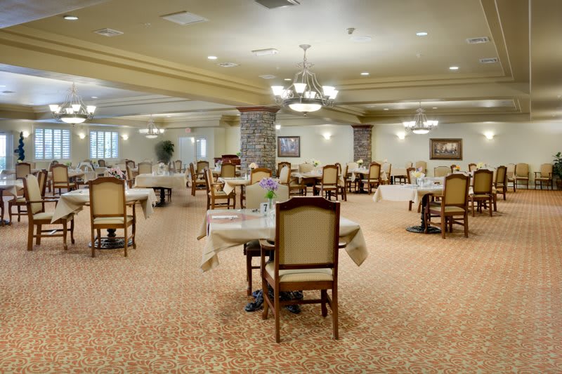 An elegant dining room with neatly arranged tables and chairs, illuminated by chandelier lighting.
