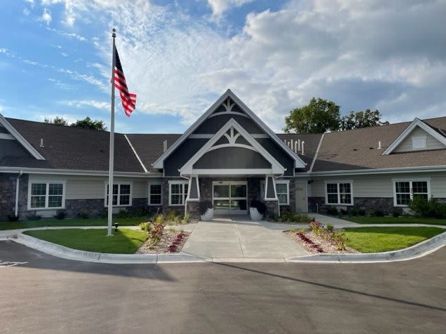 A modern building with an American flag in front, surrounded by landscaped gardens and a cloudy sky.