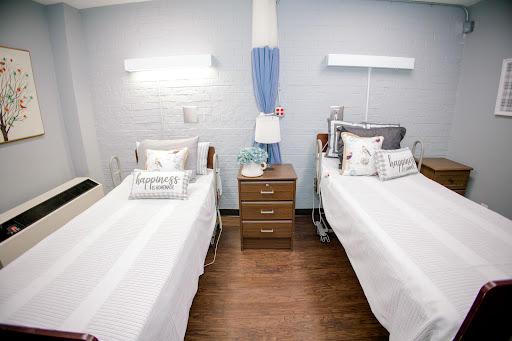 A well-organized patient room featuring two beds, each with white linens and decorative pillows.
