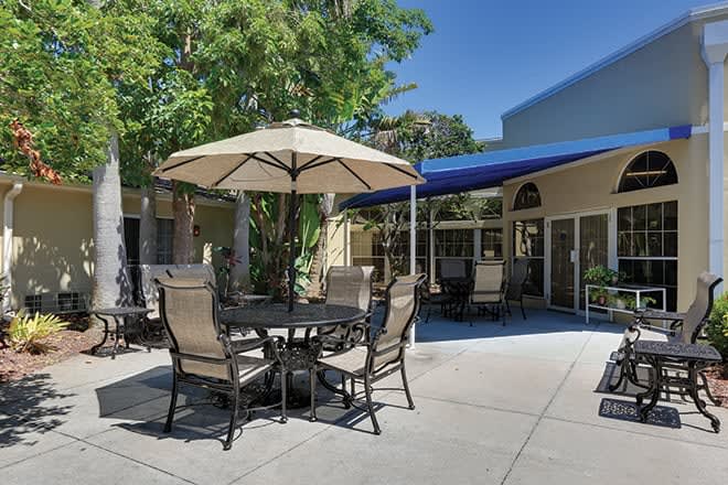 A sunny patio area with a table, chairs, and an umbrella for shade.