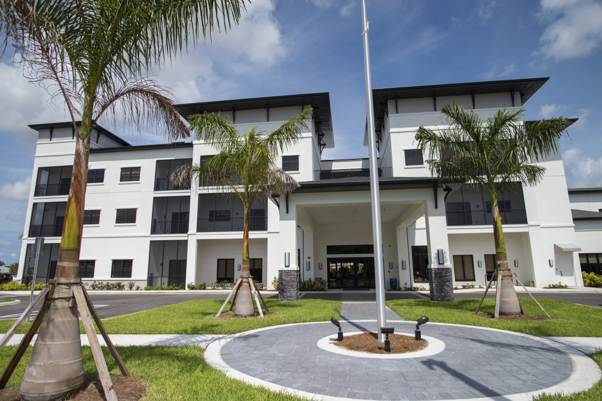 A modern building with palm trees and a flagpole at the entrance.