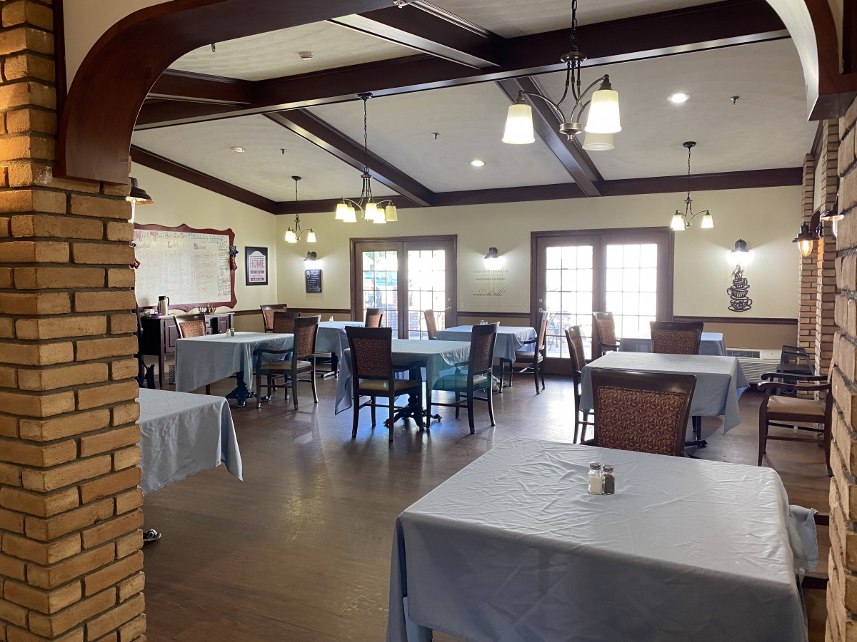 A spacious dining room with neatly arranged tables and chairs, featuring elegant lighting and wooden ceiling beams.