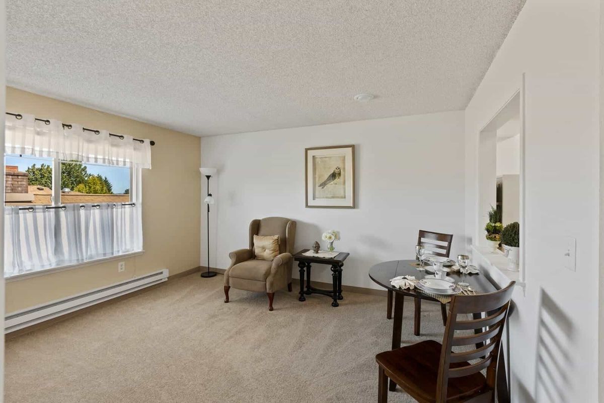 A cozy living room with a comfortable chair, a small dining table set, and a window letting in natural light.