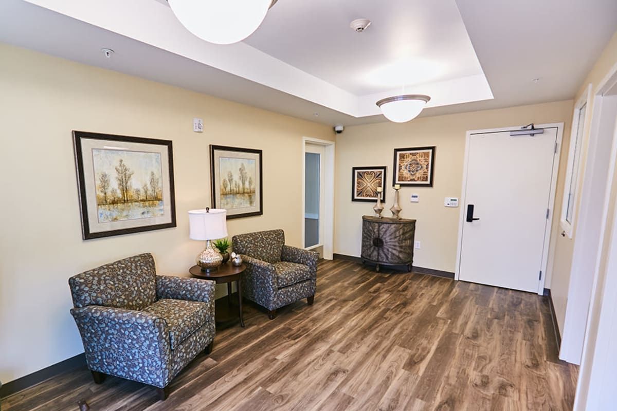 A cozy lobby area with chairs, paintings, and wood flooring.