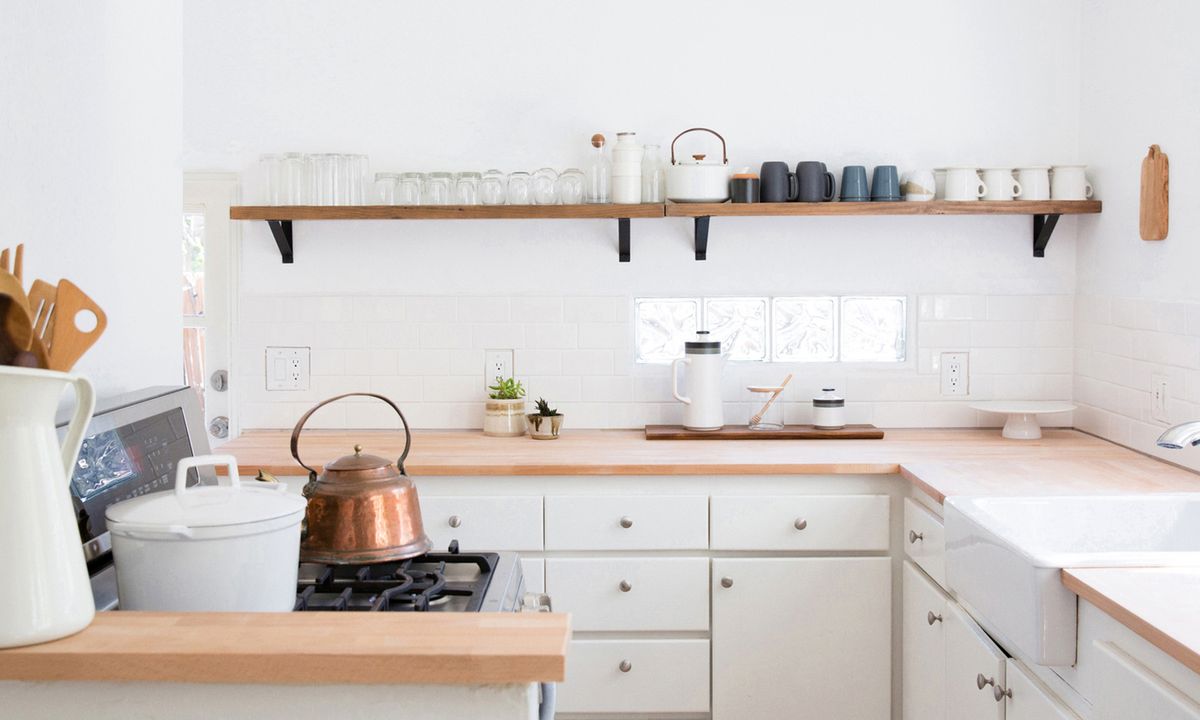 A minimalist kitchen featuring white cabinets, wooden countertops, and a copper kettle on the stove.