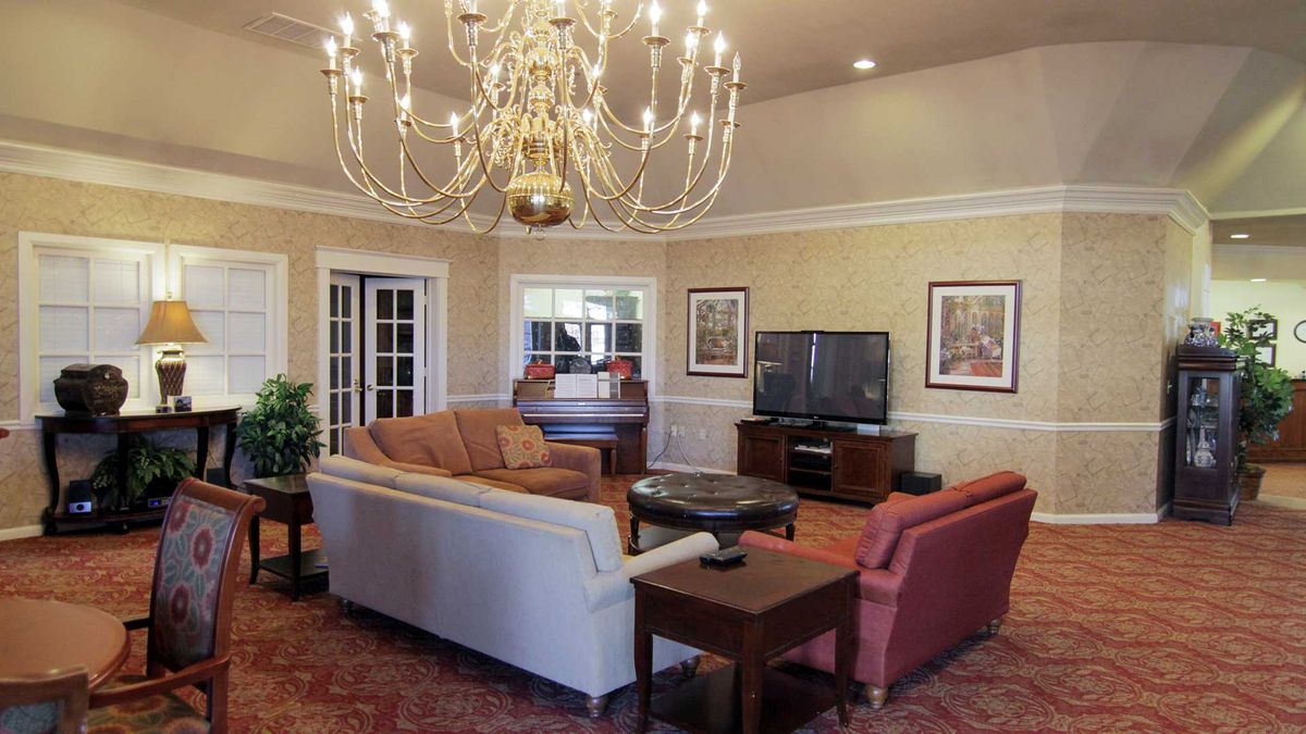 A cozy living room featuring a large chandelier, comfortable seating, and a television.