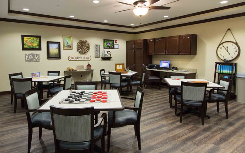 A cozy game room featuring tables with checkers, a computer desk, and wall art, all under a ceiling fan.