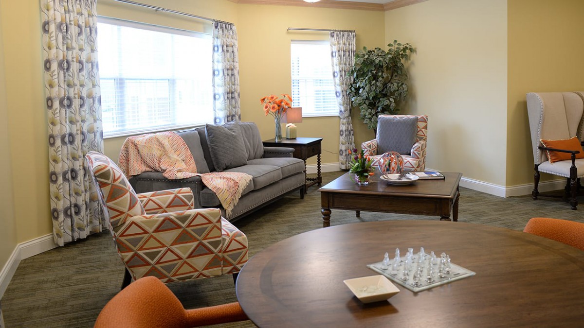 A cozy living room with a sofa, armchair, and coffee table, enhanced by colorful decor and a chessboard.