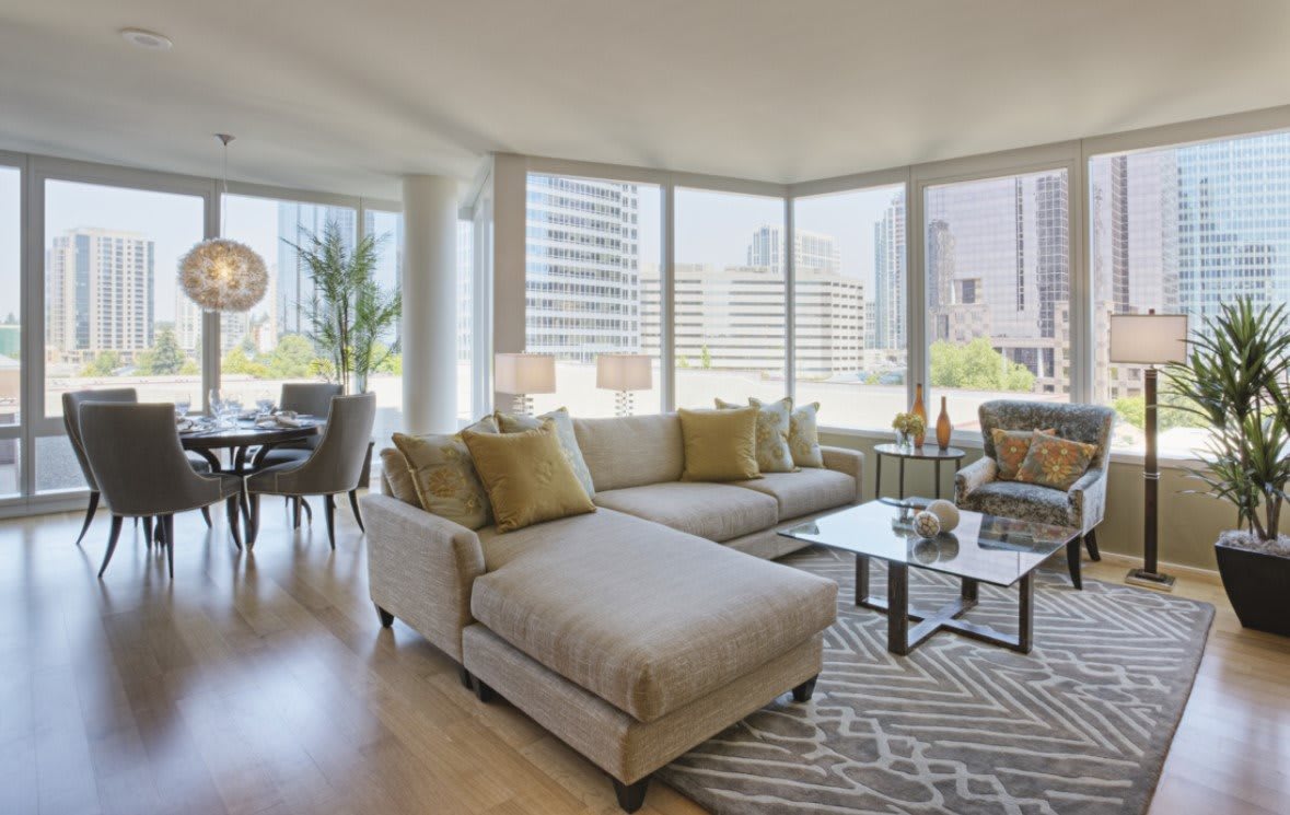 A modern living room with large windows showcasing a city view, featuring comfortable seating and a stylish coffee table.