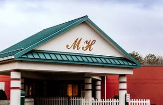 A building entrance with a green roof and the initials 'MH' displayed prominently.