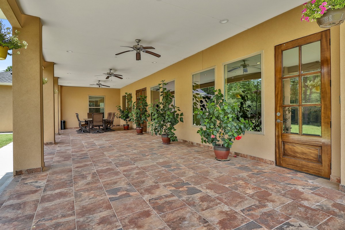 A spacious outdoor patio with tile flooring, ceiling fans, and potted plants.