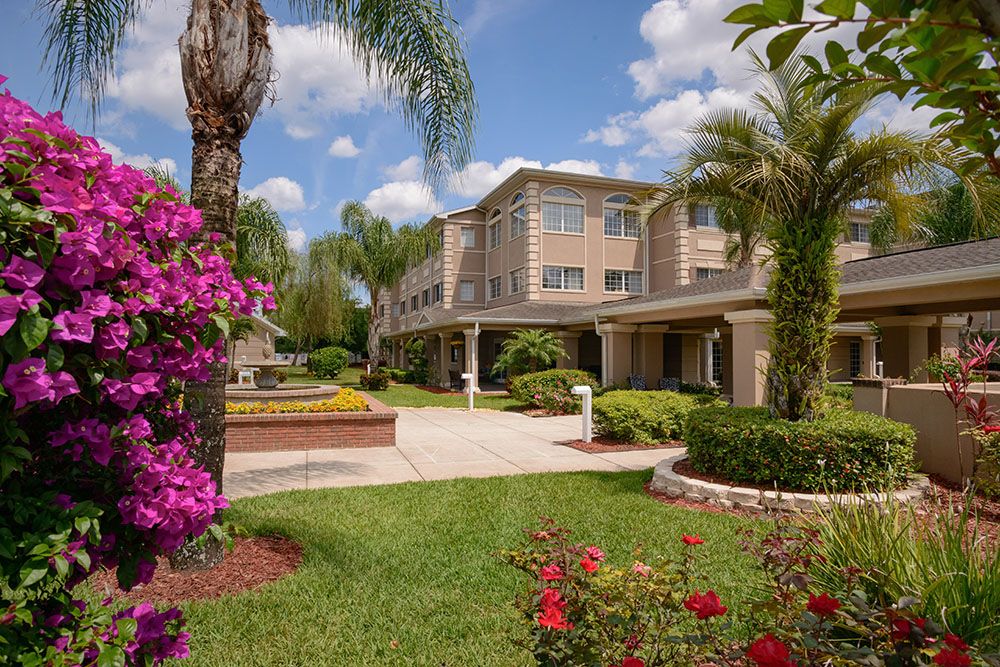 A scenic view of a building surrounded by lush gardens with palm trees and colorful flowers on a sunny day.