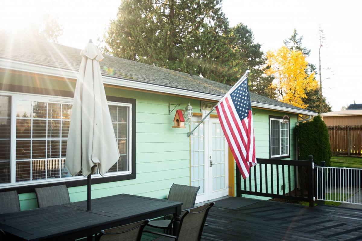 A cozy patio with outdoor furniture, featuring an American flag mounted on a mint-green house.