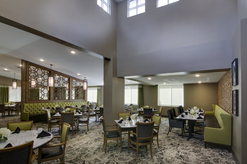 A spacious dining area with neatly arranged tables and chairs, featuring large windows and modern lighting.