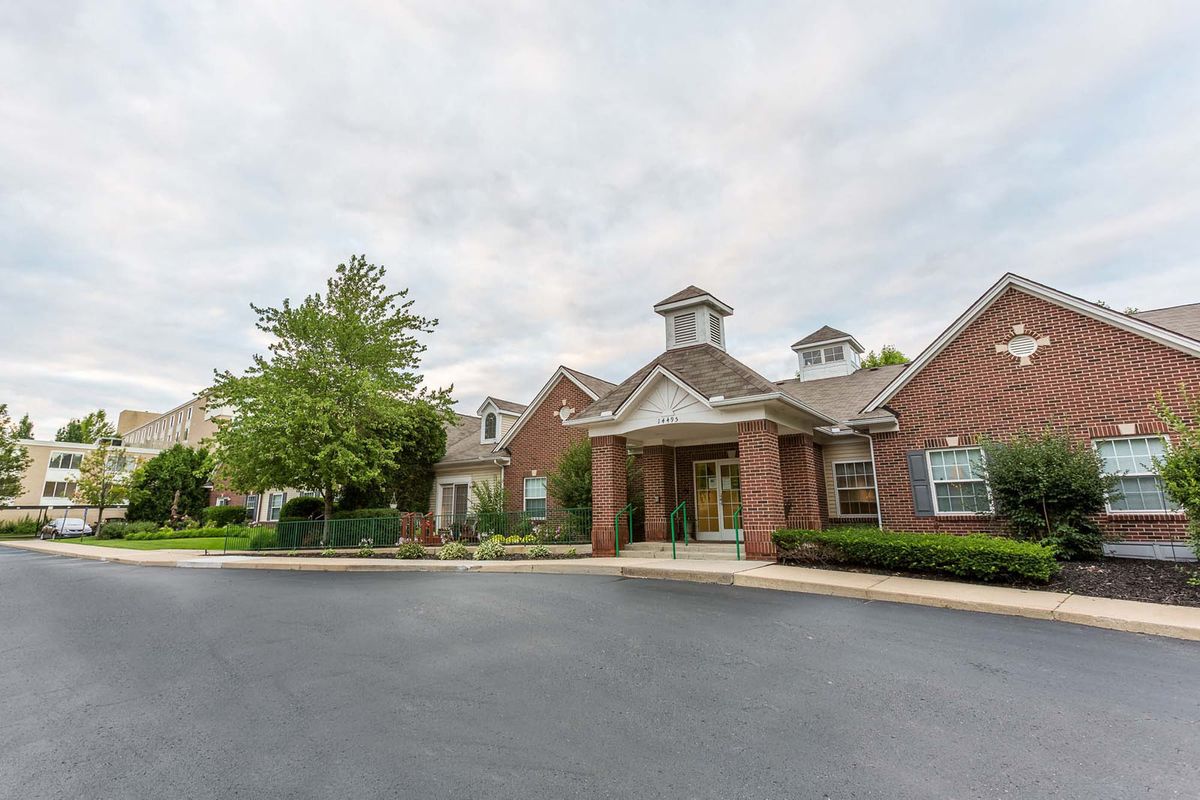 A brick residential building with a driveway and trees under a cloudy sky.