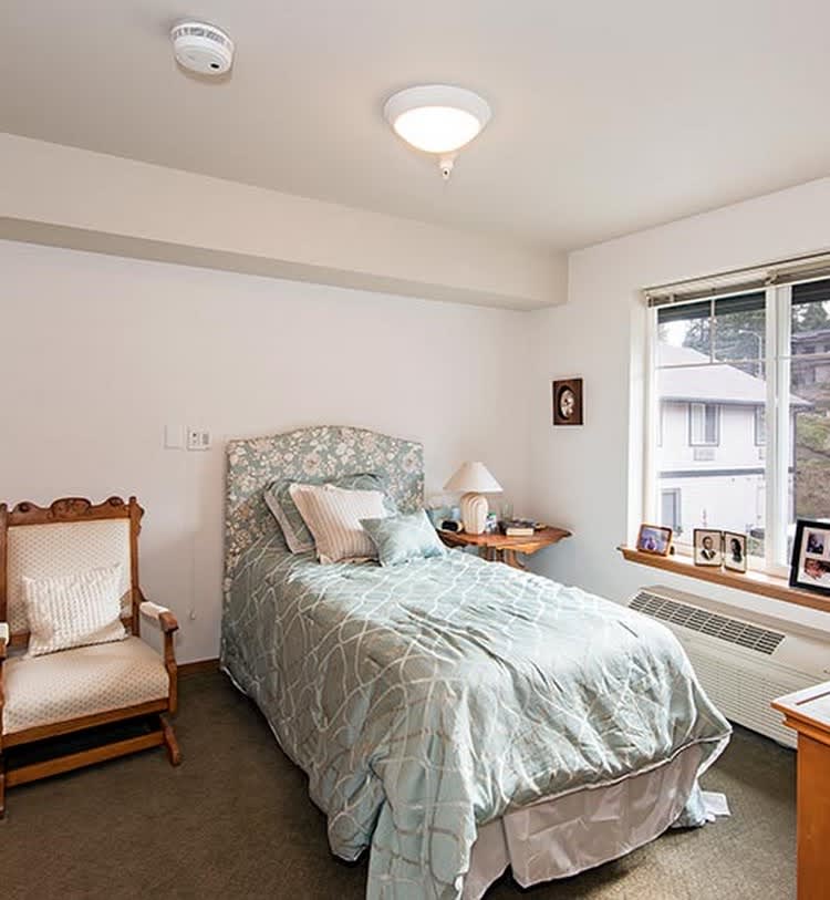 A cozy bedroom with a single bed, chair, and window view.