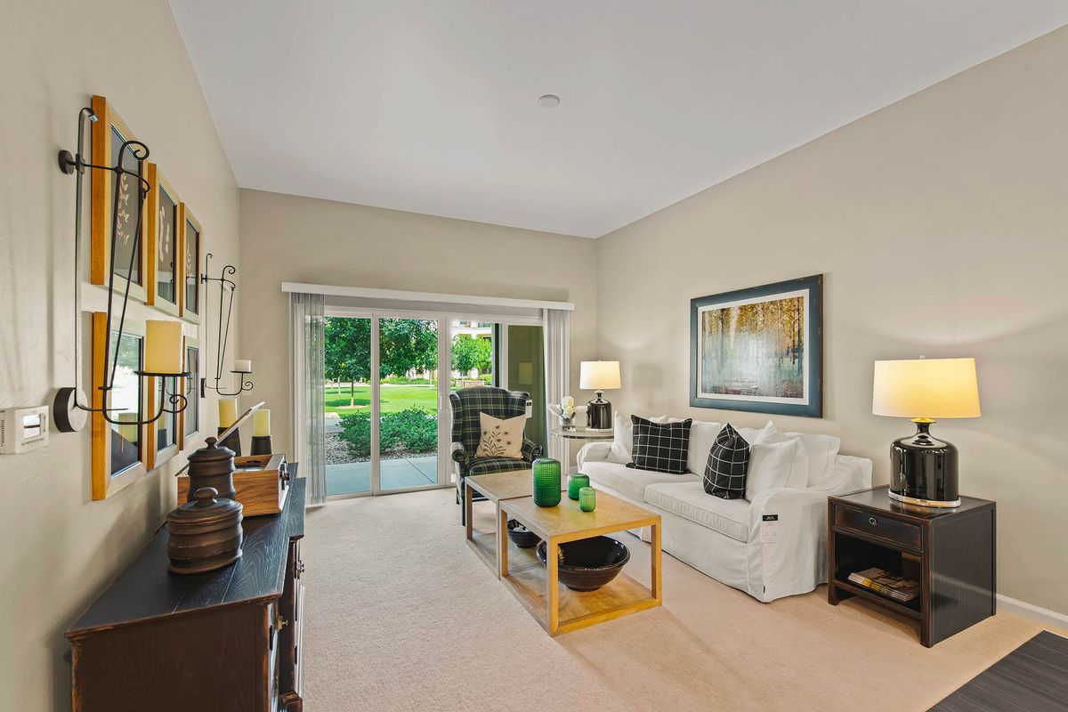 A well-furnished living room with a sofa, coffee table, and sliding glass door leading to a lush green garden.