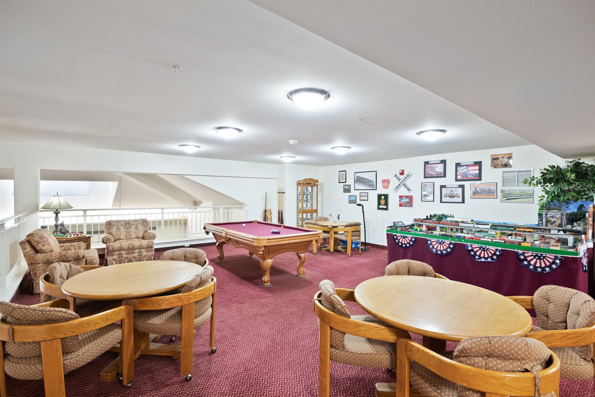 A well-equipped game room featuring a pool table, foosball table, and multiple seating areas under bright indoor lighting.