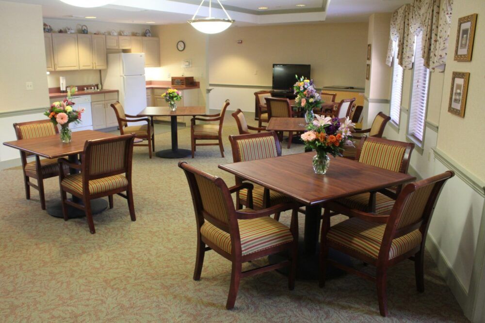 A cozy dining area with several tables and chairs, decorated with flowers on the tables.