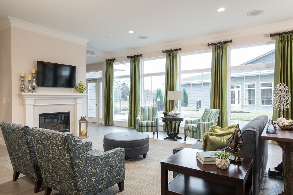 A modern living room with green curtains, comfortable seating, a fireplace, and ample natural light.
