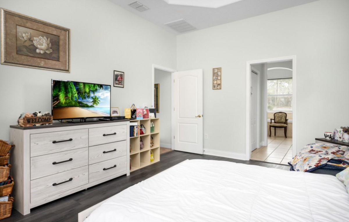 A modern and minimalist bedroom featuring a dresser with a TV, simple decor, and an open doorway leading to another room.