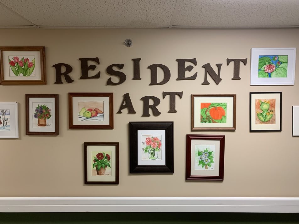 A display of resident artwork featuring framed paintings of flowers on a wall.