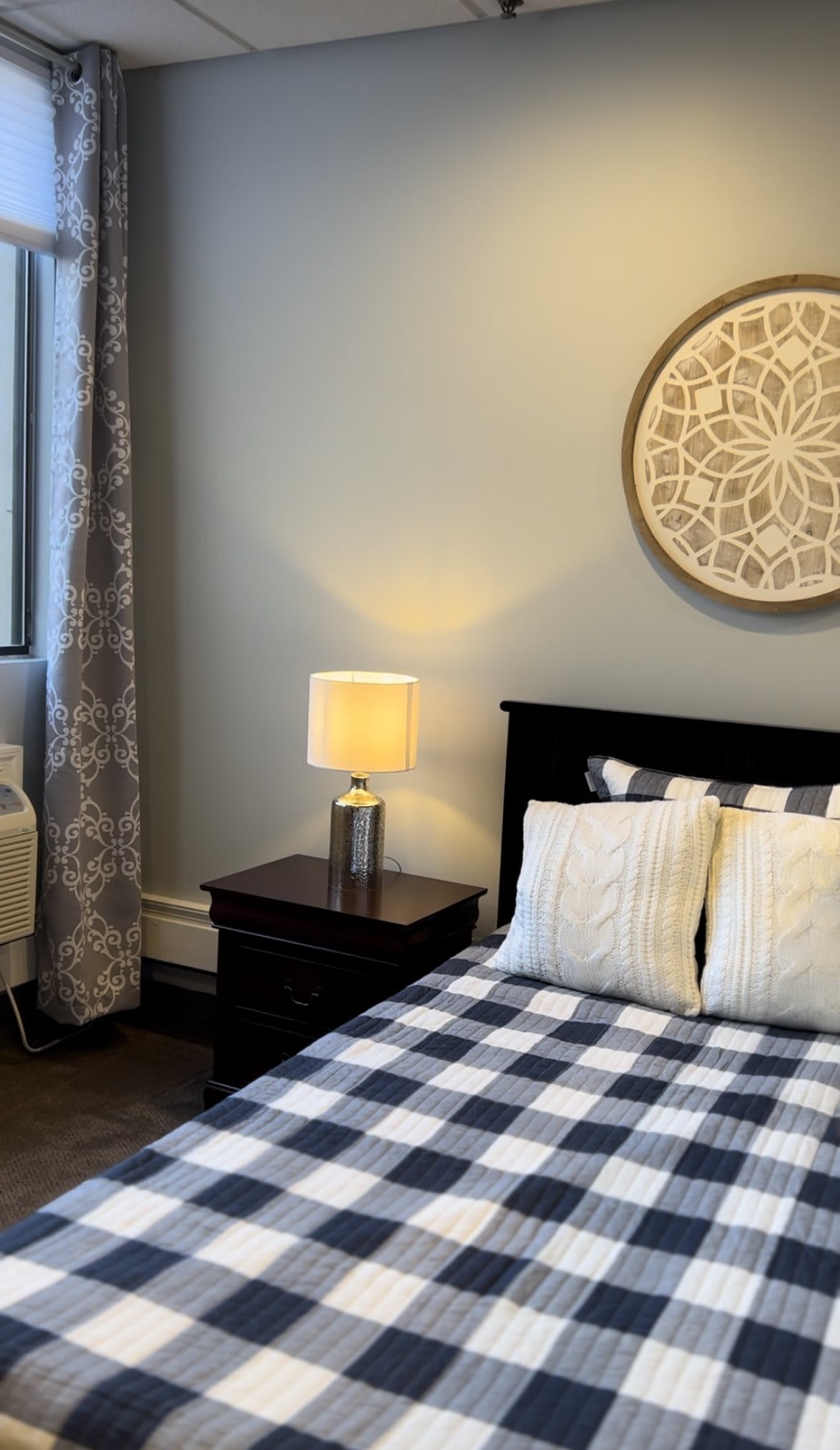 A cozy bedroom with a checkered bedspread, decorative pillows, a bedside lamp, and wall art.