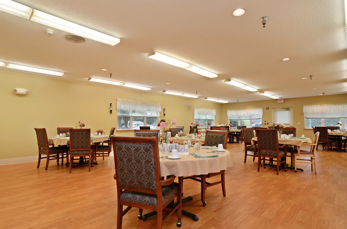 A spacious dining area with neatly arranged tables and chairs, featuring warm lighting and a wooden floor.