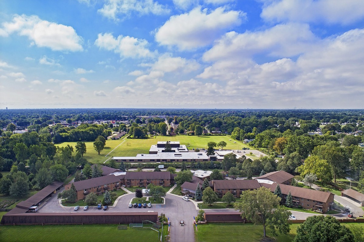Aerial view of a campus surrounded by greenery under a partly cloudy sky.