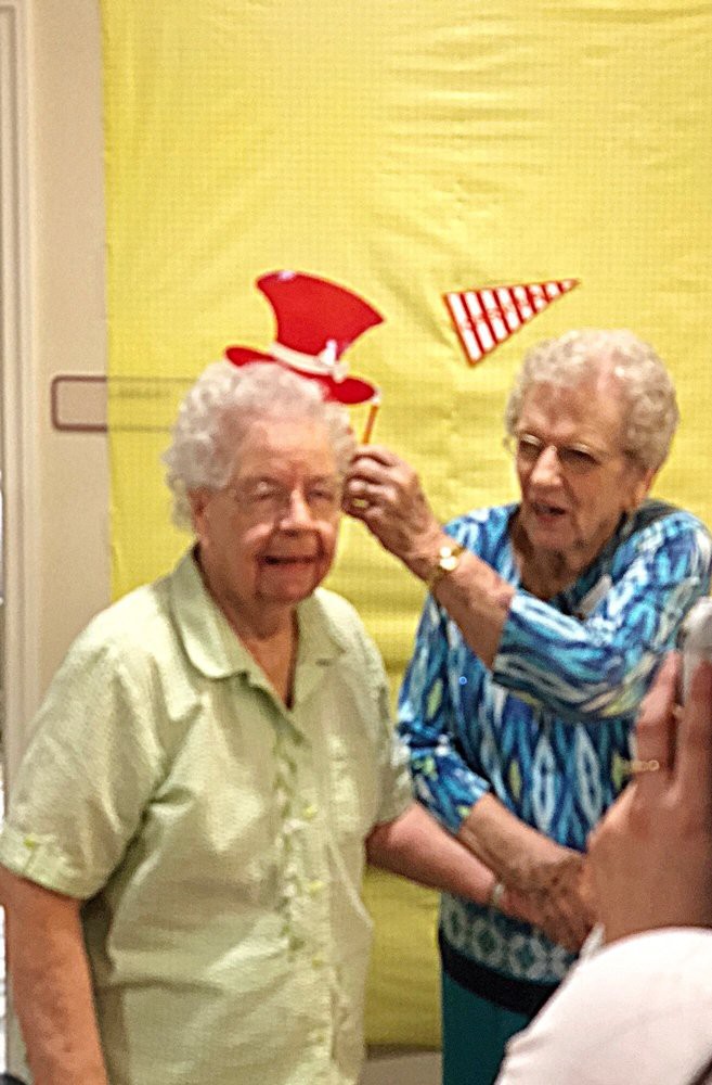 Two elderly women having fun at a celebration, playfully arranging party hats.