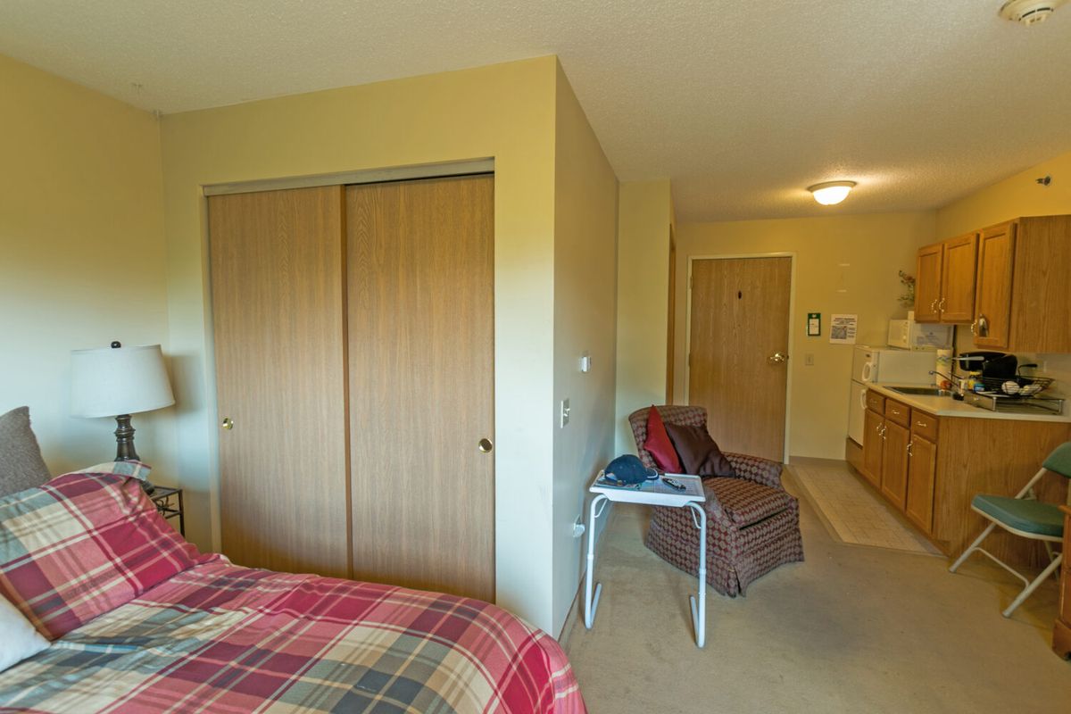 A cozy bedroom with a plaid bedspread, wooden closet doors, and comfortable seating.
