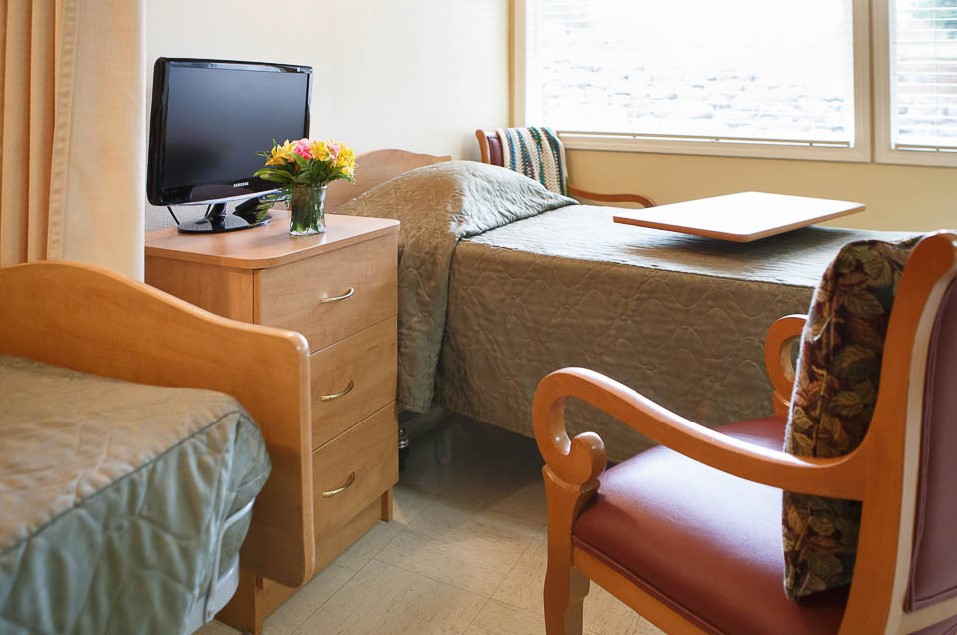A cozy bedroom with a TV, dresser, and flowers on the side table.