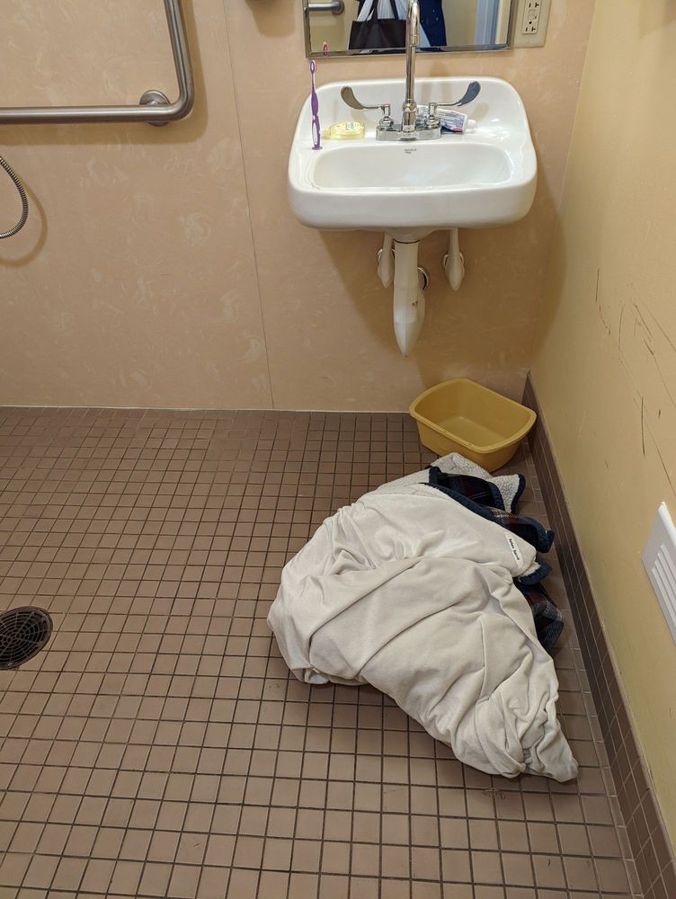 A bathroom with a tiled floor, featuring a sink and a bundle of clothes on the ground.