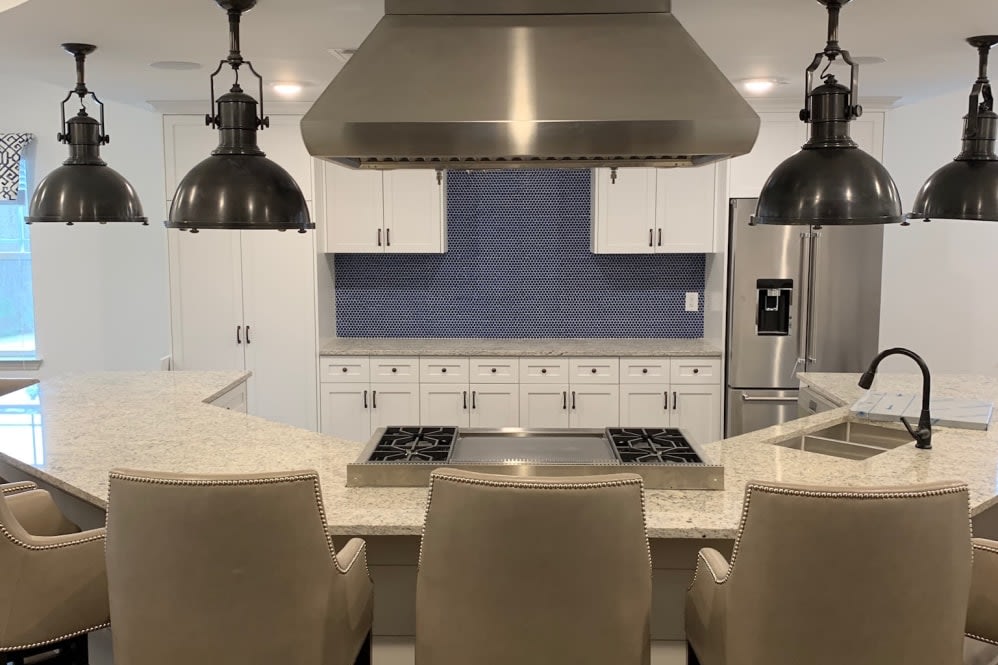 A modern kitchen with sleek countertops, blue tile backsplash, and stylish lighting.