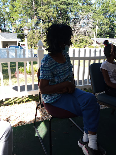 A woman seated outdoors wearing a mask, enjoying the sunlight.