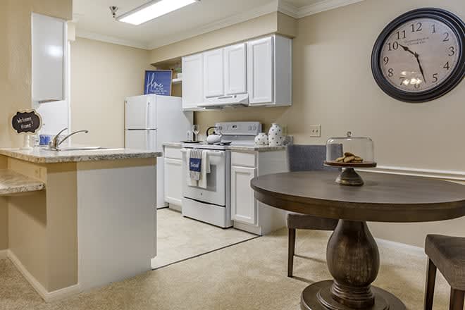 A modern kitchen with white cabinets and appliances, including a fridge and stove, adjacent to a dining table.
