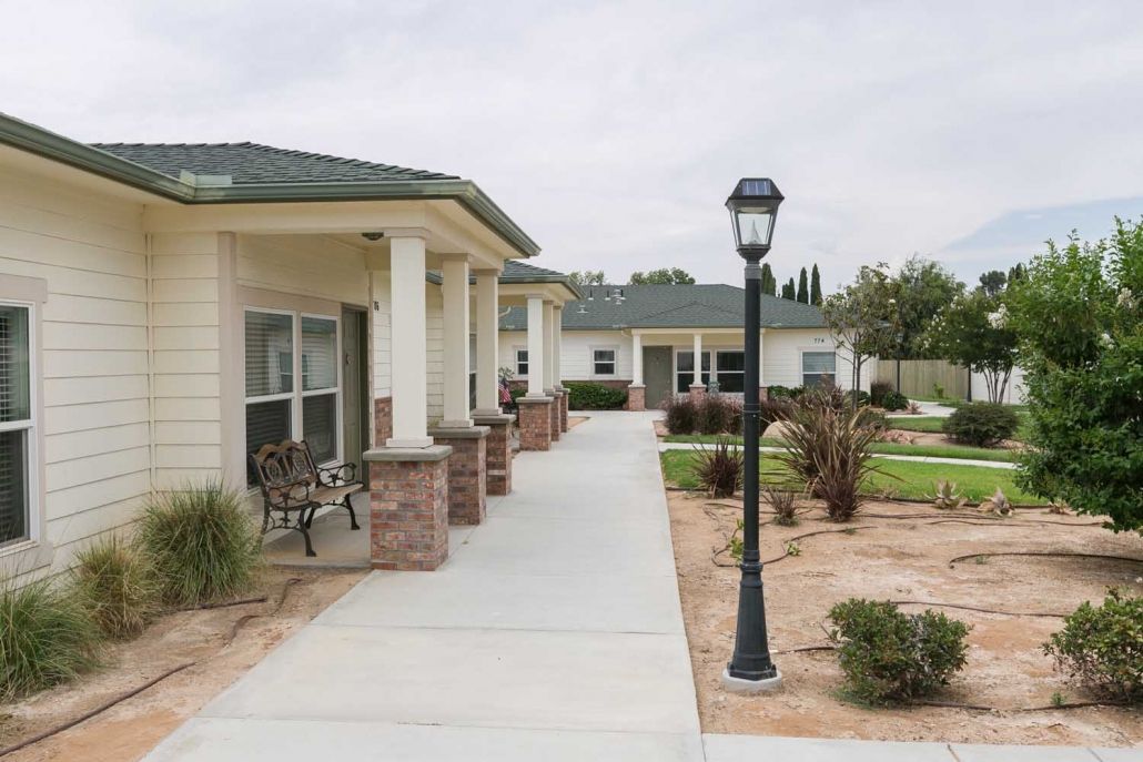 A walkway leading to residential buildings, lined with a garden and lamppost.
