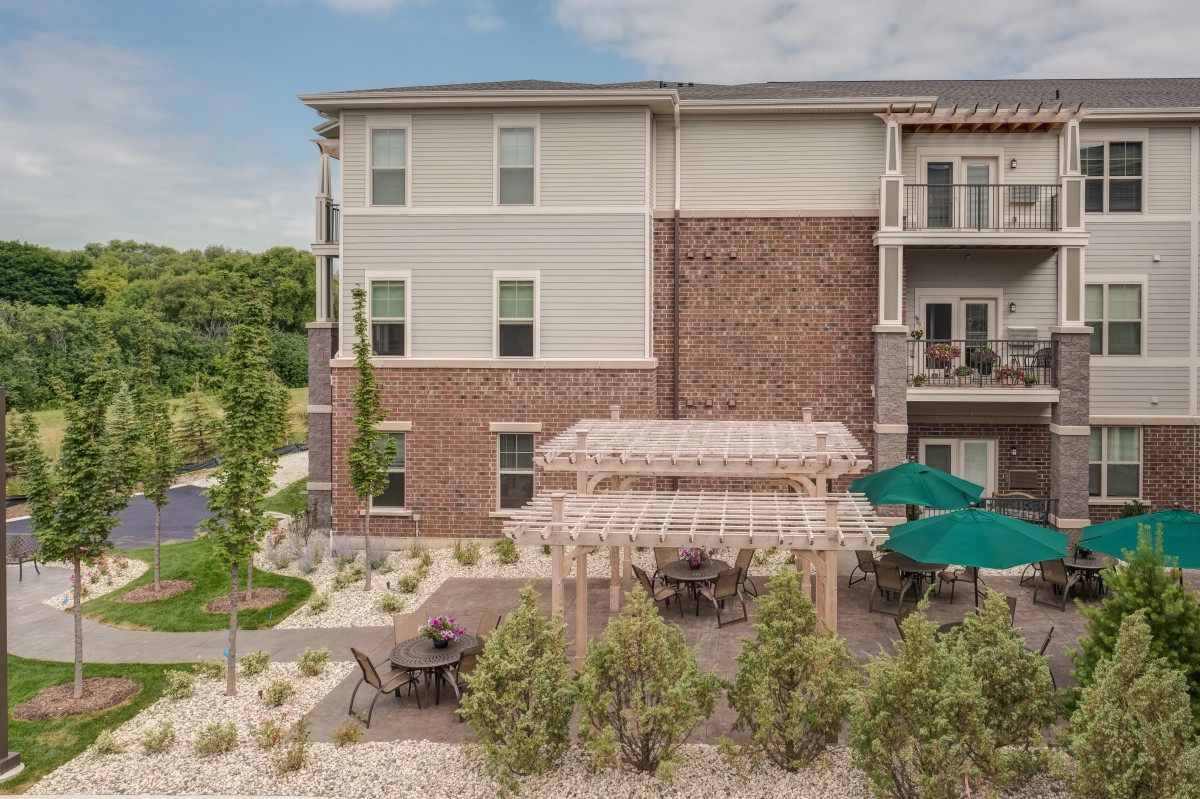 A modern apartment building with an outdoor patio and shaded seating area surrounded by greenery.