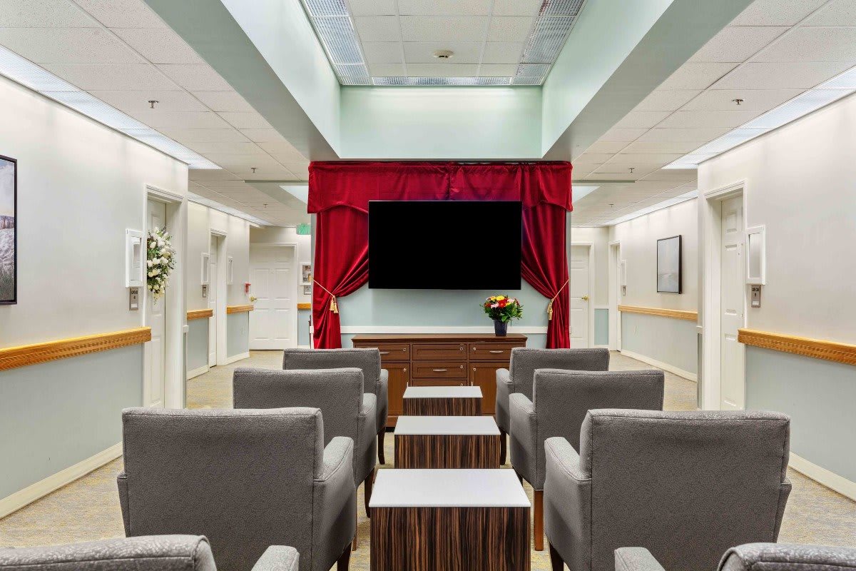 A cozy indoor theater setup with gray chairs facing a large screen with red curtains.